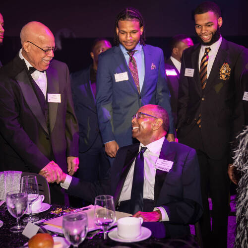 Standing at left, Don Willams Sr. chats with William Pickard who is seated at a table during Enrichment Dinner 2022.